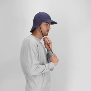 A navy Fraser Cap worn by a man in a grey sweatshirt, featuring a chin strap and a wide brim.