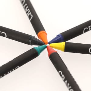 A crayon set featuring six crayons in red, yellow, blue, green, orange, and black, arranged in a circular pattern.