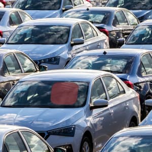 A red sunshade is placed on the windshield of a silver car, surrounded by several other parked silver cars.
