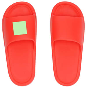 A pair of bright red flip flops with a single green square on one strap. They have a simple design and a logo.
