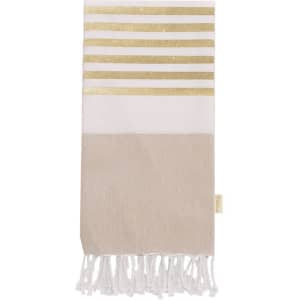 A bath towel in white and beige, featuring gold stripes and tasselled ends, with branding present.
