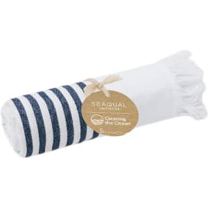 A rolled towel with blue and white stripes, featuring fringe edges and a tag indicating an eco-friendly initiative.