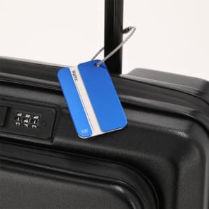 A blue luggage tag attached to a black suitcase with a combination lock. It has a branding logo.