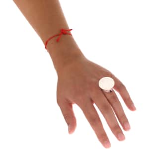 A hand wearing a large silver ring with a smooth dome surface, accompanied by a simple red bracelet.