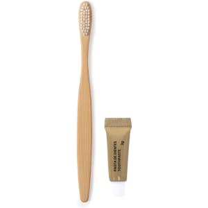 A bamboo toothbrush with a textured head beside a small tube of golden toothpaste. Both items are in a natural style.