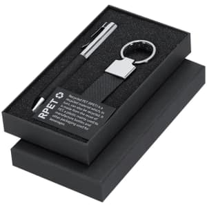 A black gift box containing a pen and a silver keyring, with a textured black strap, both resting on a foam insert.