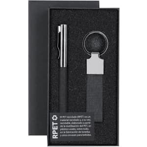 A gift box containing a silver pen and a black keyring, presented on a black textured background.