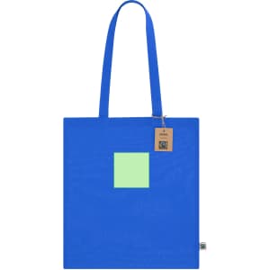A bright blue tote bag with a green square patch and a tag. It features sturdy handles for carrying.