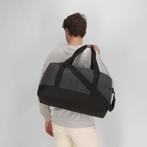 A grey and black duffel bag is being carried by a person, featuring adjustable straps and a shoulder strap.