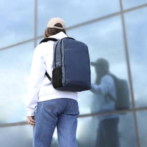A person wearing a white hoodie and cap carries a blue and black Galix Backpack against a reflective background.