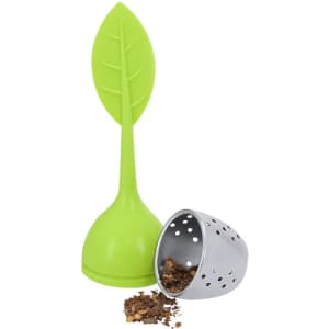 A green leaf-shaped tea infuser sits beside a silver mesh ball infuser with loose tea scattered nearby.