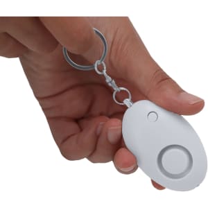 A white personal alarm keychain is held in a hand, featuring a round button and keyring attachment.