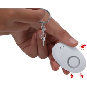 A white personal alarm held in a hand, attached to a keyring, featuring a circular activation button.