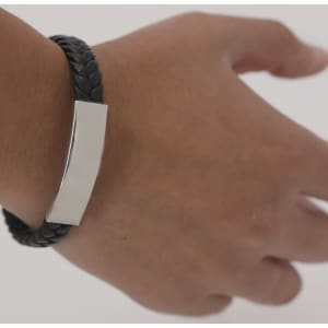 A black braided bracelet with a shiny silver rectangular centrepiece on a wrist.