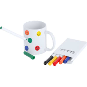 A white mug with smiley face stickers, accompanied by a green marker and a set of five vibrant markers: red, yellow, black, green, and blue.