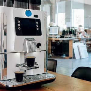 A coffee machine with a sleek silver design, serving two cups of coffee on a counter in a modern workspace.