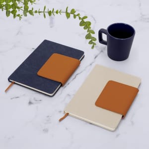 Two notebooks with orange accents, one in blue and one in cream, placed on a marble surface alongside a dark blue mug.