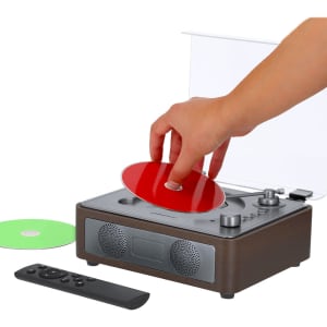 A CD player in brown with a hand placing a red disc, alongside a green disc and a remote control.