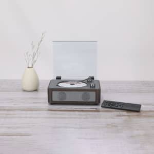 A brown CD player with a transparent cover, accompanied by a remote, sits on a wooden surface.