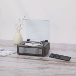 A brown CD player with a transparent lid, remote control, and decorative vase on a wooden surface.