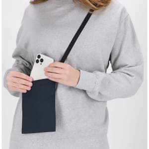 A person in a grey sweatshirt holds a navy multipurpose bag, inserting a mobile phone into it. The bag has a strap and a logo.