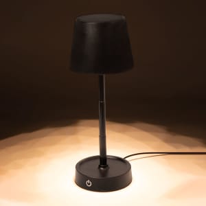 A black lamp with a cylindrical base and a tapered shade, emitting a warm light in a dim setting.
