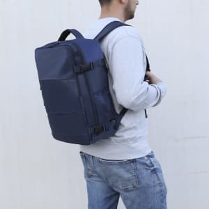 A navy blue backpack with multiple compartments, being worn on the back by a person in a grey sweatshirt.