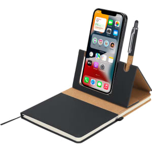 A black notepad holder featuring a phone stand, cork accents, and a pen. It includes an open notepad.