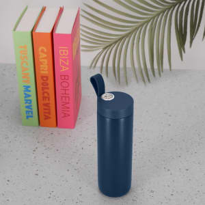A drink bottle in navy blue with a lid, featuring a small logo, placed beside colourful books on a table.