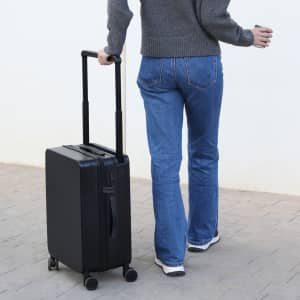 A black wheeled bag with an extendable handle, being pulled by a person in grey and blue attire.
