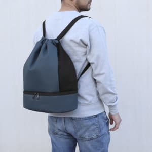 A person wearing a blue and black backpack with drawstring and zippered sections. The backpack features a mesh panel.