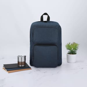 A navy blue backpack with multiple pockets, placed near a notebook, a drink bottle, and a small potted plant.