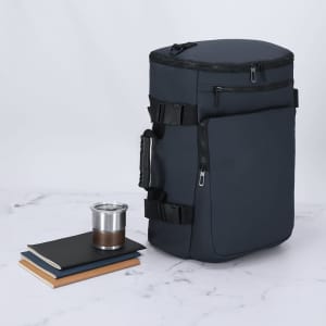 A dark grey backpack with zippers and straps, accompanied by a cup and notebooks on a marble surface.