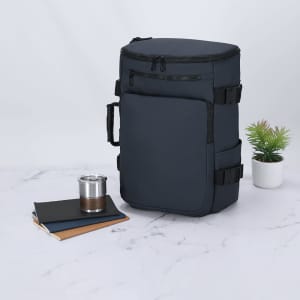 A navy blue Rigan Backpack with adjustable straps, accompanied by a drink bottle, notebooks, and a small plant.