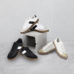 Four pairs of trainers in black, white, and a speckled design, displayed on a grey concrete block. Each pair has a logo.