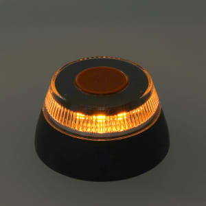 An emergency light with an orange light and a black base, featuring a circular design and a central button.