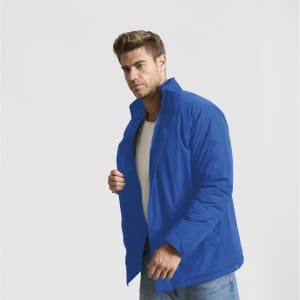 A man wearing a bright blue puffer jacket, styled casually with a white shirt and jeans. The jacket features a collar and has a logo.
