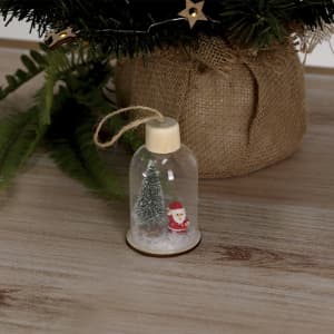 A small glass dome decoration featuring a green tree and a Santa figure, set on a wooden base, with twine for hanging.