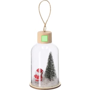 A decorative glass dome featuring a miniature Santa and a green tree, with a wooden base and a hanging twine.