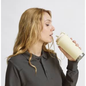 A drink bottle in cream colour, featuring a straw and a metallic base, held by a person with wavy hair. It has a logo.