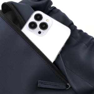 A navy drawstring bag with a smartphone partially visible in an outer pocket, featuring a logo.