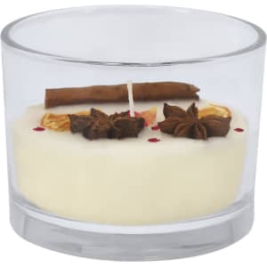A scented candle in a clear glass holder, featuring white wax, cinnamon stick, and decorative spices.