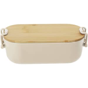 A beige lunch box with a bamboo lid and white clasps, featuring a sleek, rounded design and a logo.