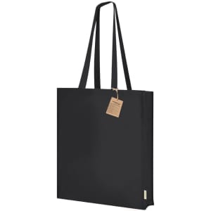 A black tote bag with two long handles and a tag attached. The bag features a simple, minimal design and a logo.