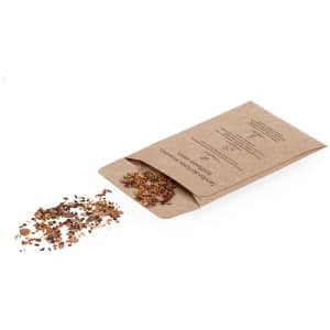 A brown paper seed packet with a sprinkle of assorted seeds on a white surface. It features a logo.