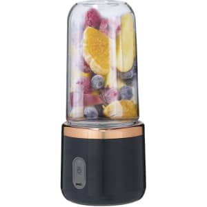 A black and copper blender with a clear container filled with various fruits, including oranges, berries, and bananas.