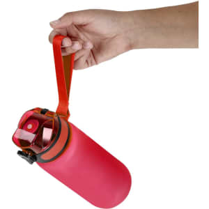 A pink drink bottle with an orange strap is being held by a hand, featuring a secure cap and a logo.