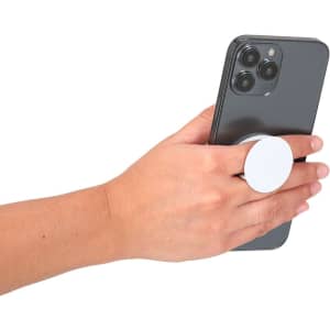 A hand holds a smartphone with a white circular phone stand attached. The phone is dark in colour.