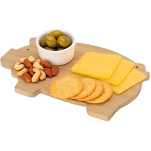 A wooden cutting board in the shape of a pig, featuring cheese slices, crackers, nuts, and a small bowl of olives.