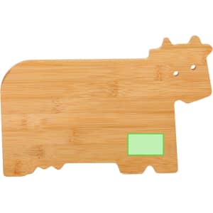 A bamboo cutting board shaped like a cow, featuring a green rectangular area and two holes for eyes.